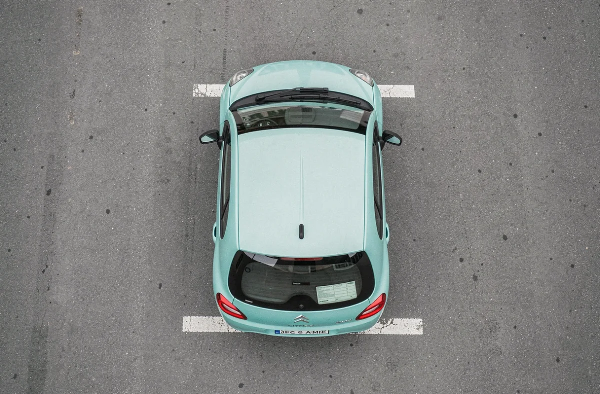 Vue aérienne de dessus d'une Citroën Ami sur asphalte gris, silhouette carrée compacte et carrosserie turquoise
