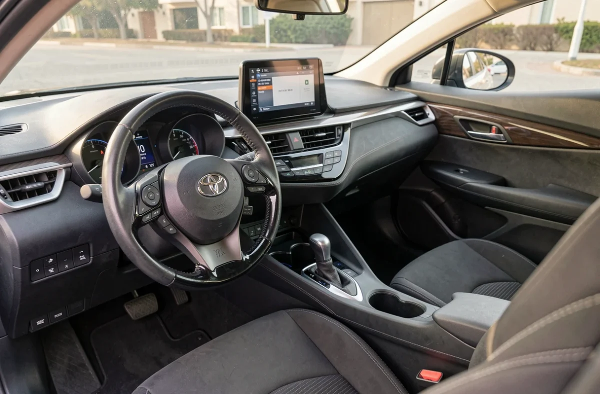 Intérieur du Toyota C-HR montrant le tableau de bord compact, l'écran tactile central et les sièges en tissu noir avec surpiqûres